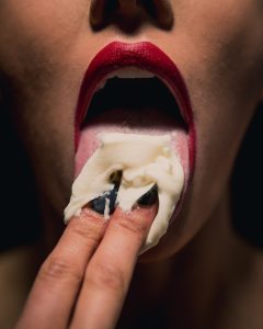 seductive female with cream on her tongue and mouth open with red lipstick